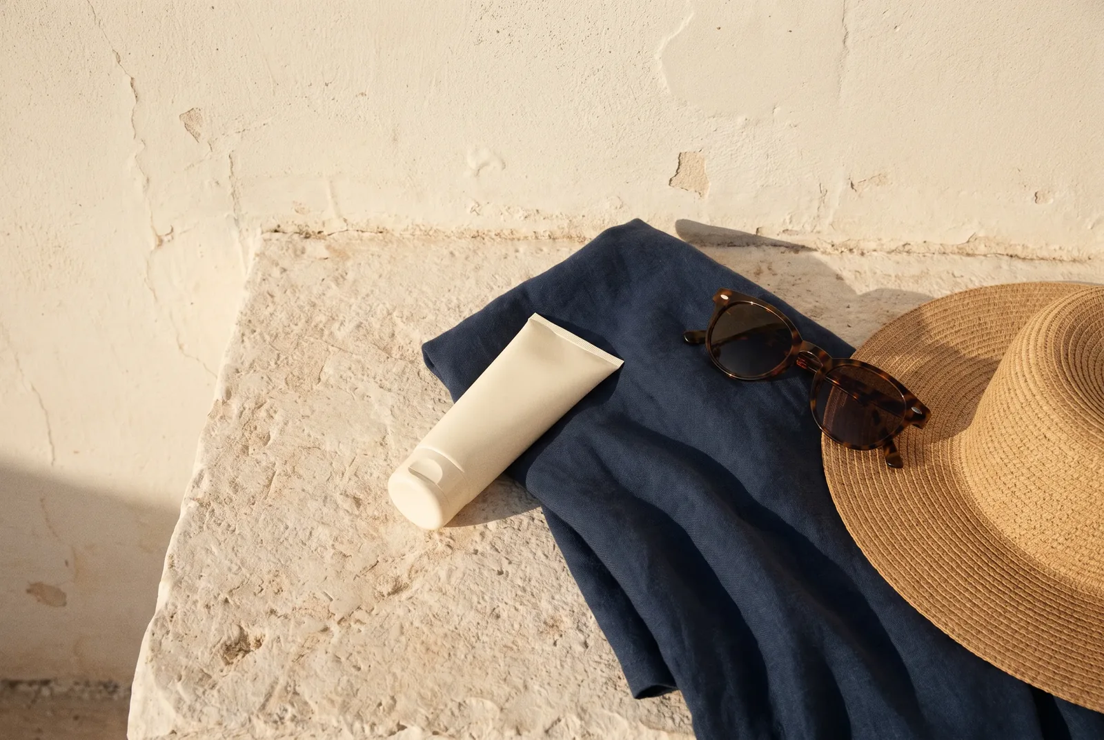 Protector solar, sombrero y gafas sobre una superficie clara